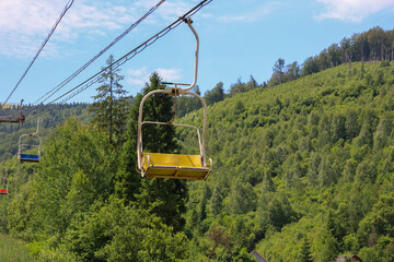 A view of a mountain slope covered with a dense forest, over which chairlift lines pass. Under the...