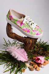 Floral sneaker with pink tulips, feather, seashell, and grass on studio background