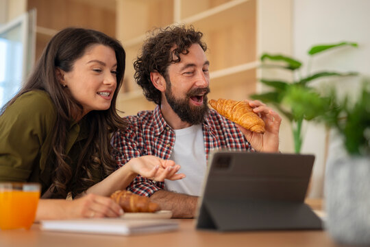 Young couple eating pizza and watching something on a tablet at home.
 - Powered by Adobe