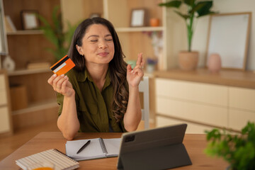 Woman holding an orange credit card and looking thoughtfully in a modern apartment
