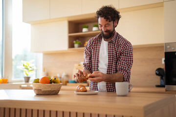 Bearded man slicing fresh bread in a modern kitchen with fruit basket and coffee cup on the...