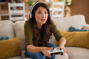Young woman wearing headphones with focused and surprised expression while playing video games at home.
