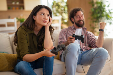 Frustrated woman holding video game controller while man celebrates victory at home.

