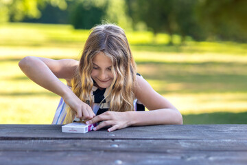 Joyful young girl unwrapping Dubai chocolate in nature on a wooden table at sunset. Laughing woman with angel chocolate gift