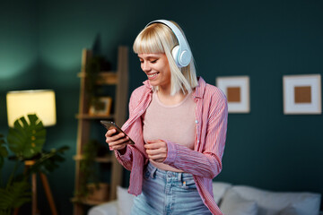 Happy young woman listening to music on headphones and dancing at home