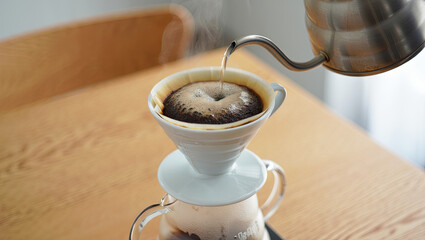 A person is carefully pouring hot water over freshly ground coffee in a dripper, creating aromatic...