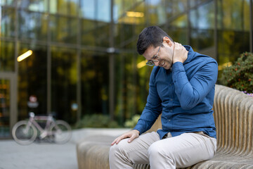 A man is experiencing neck pain, sitting on a bench outdoors, possibly from a strained muscle.
