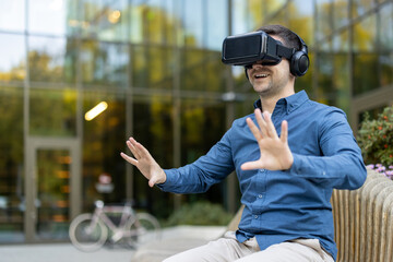 A man experiences virtual reality outdoors, wearing VR glasses and gesturing with hands.
