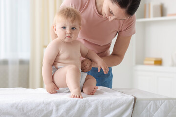 Mother changing her baby's diaper on table at home