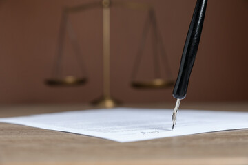 Signing notary document with fountain pen at wooden table against brown background, closeup