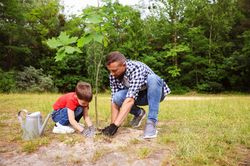 Father and his son planting tree into soil outdoors