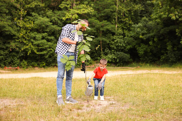 Father and his son planting tree into soil outdoors