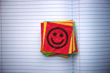 A stack of colorful paper notes with a happy face on one of them in an open notebook. Close up.