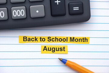 Yellow strips of paper with the words Back to School Month - August typed on them lying in an open notebook near a calculator and ballpoint pen. Close up.