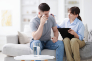 Psychologist supporting patient during therapy session in office, focus on glass of water