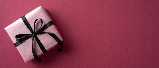 Elegant pink gift box with a black ribbon placed on a vibrant pink surface