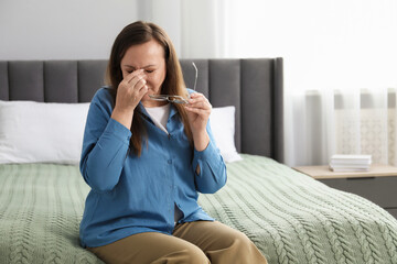 Woman with glasses suffering from eyestrain on bed at home, space for text