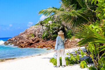 Woman on a tropical beach with palm trees and rocky coastline