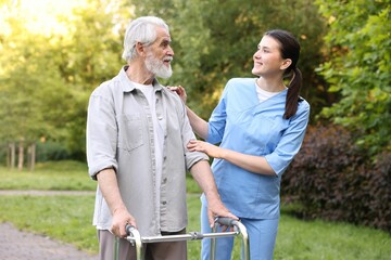 Smiling nurse supporting elderly man who using walking frame outdoors
