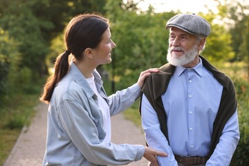 Caregiver supporting elderly man in summer park