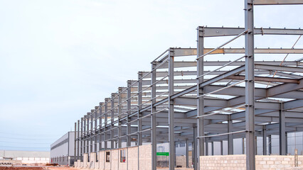 Metal structure of warehouse industrial factory building in construction site against gray sky background in industry settlement area, Perspective side view with copy space