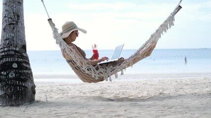 Woman in a straw hat relaxes in a hammock on a tropical beach while working on laptop. She sips a cool watermelon shake, embodying the digital nomad lifestyle - Powered by Adobe