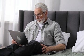 Senior man with vision problem using laptop on bed at home