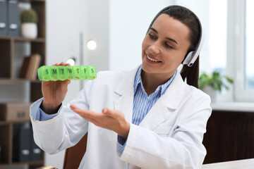 Doctor in headphones with pill box having online consultation indoors