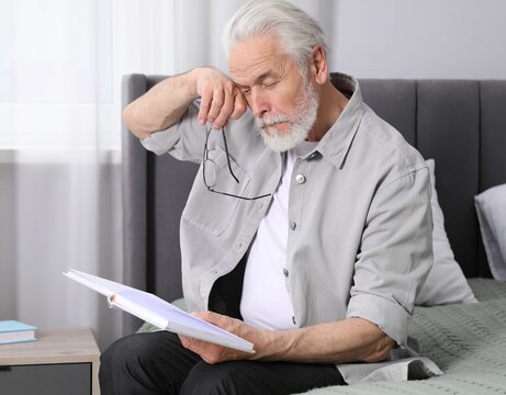 Senior man with vision problem reading book on bed at home