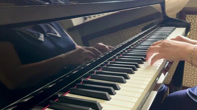 Top-down view of a person playing a digital Casio piano with both hands. The keys and hands are clearly visible, and sheet music is placed above the keyboard. 