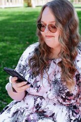 Young woman with long curly hair using a smartphone outdoors in a park on a sunny day, smiling and...