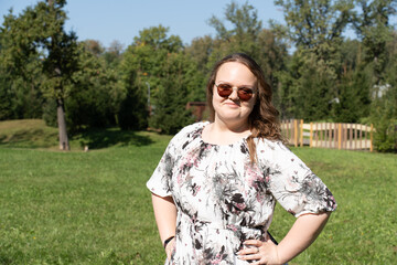 Smiling young woman with long curly hair and sunglasses standing outdoors on a sunny day, looking at the camera.