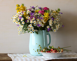 Wildflowers bouquet in light blue jug and wild strawberries on rustic table