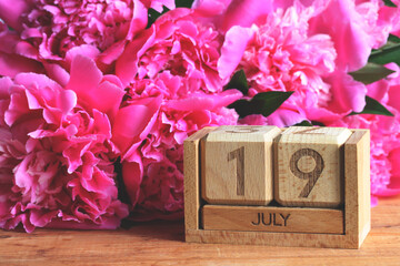 Pink peonies and wooden calendar showing july 19th, summer concept