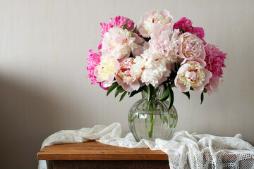 Bouquet of pink and white peonies in glass vase bringing elegance to rustic interior