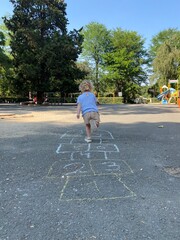 Toddler playing hopscotch alone on an empty playground on a sunny summer day. Traditional chalk...