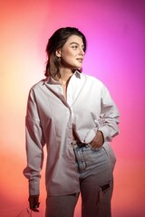 A woman in jeans and a white shirt poses on colored background in studio