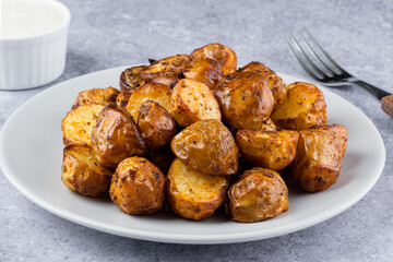 Golden brown roasted baby potatoes arranged neatly on a plate beside a small bowl of creamy dipping...