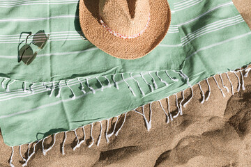 Green towel, straw hat, sunglasses on beach sand background. Aesthetic lifestyle, summer vacation...