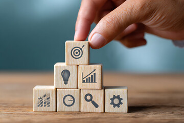A hand carefully placing a light brown wooden block with a dark gray target symbol onto a pyramid structure of similar blocks each