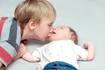 Big brother lovingly kissing his little newborn infant baby sister girl.older kid meeting new sibling,lay in bed together.Family with children at home.Love,tenderness