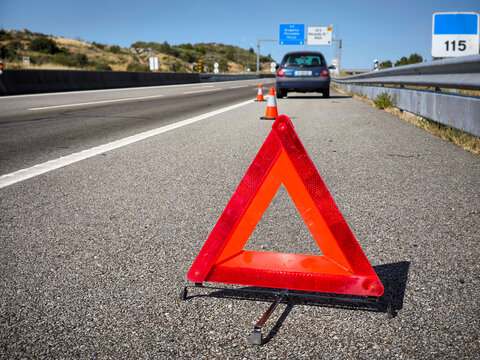 Tri&acirc;ngulo de sinaliza&ccedil;&atilde;o de emerg&ecirc;ncia na berma de uma autoestrada com um carro avariado ao fundo