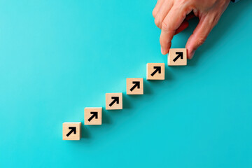 Hand Placing Wooden Block with Arrow on Teal Background, Symbolizing Progress, Growth, and Strategic Planning in Business and Personal Development, Achieving Goals