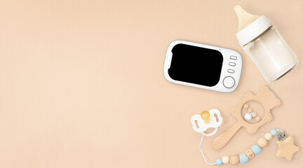 Beige background with baby monitor, bottle, pacifier, and rattle.