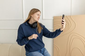 Young female blogger woman recording vlog video with mobile phone or live streaming. Content creator making selfie and sitting on the coach at home indoors