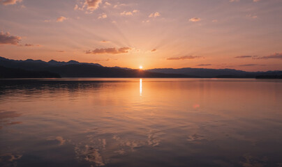 Obraz premium Golden sunset rays painting the tranquil lake as mountains watch over in serene beauty with soft