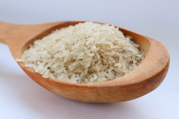 White rice in a wooden spoon on white background, close-up — concept of natural nutrition, visual purity and culinary simplicity for healthy lifestyle
