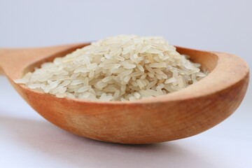 White rice in a wooden spoon on white background, close-up — concept of natural nutrition, visual purity and culinary simplicity for healthy lifestyle