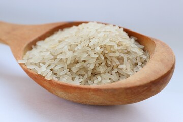 White rice in a wooden spoon on white background, close-up — concept of natural nutrition, visual purity and culinary simplicity for healthy lifestyle