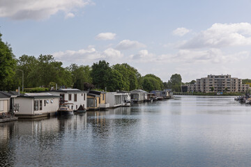A peaceful Dutch canal scene, with various houseboats lining the tranquil waters. In the distance,...